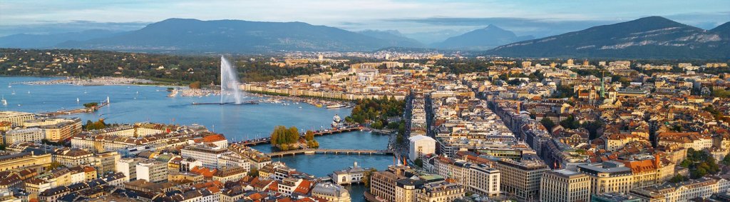 Die Stadt Genf mit dem berühmten Jet d'Eau, einem Wasserstrahl, der hoch aus dem Genfersee sprüht. Im Hintergrund sind die umliegenden Gebäude und Berge sichtbar. | La ville de Genève avec le célèbre Jet d'Eau, un jet d'eau qui s'élève haut dans le lac de Genève. En arrière-plan, on peut voir les bâtiments environnants et les montagnes. | The city of Geneva featuring the famous Jet d'Eau, a water fountain that shoots high into Lake Geneva. In the background, the surrounding buildings and mountains are visible.