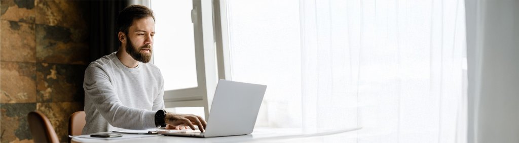 Ein junger Mann arbeitet zuhause an seinem Laptop. | A young man is working on his laptop at home. | Un jeune homme travaille chez lui sur son ordinateur portable.